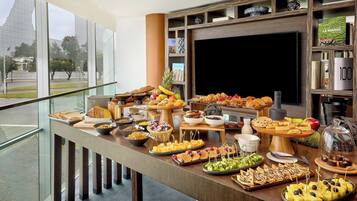 Una mesa de buffet con diferentes alimentos y un televisor al fondo.