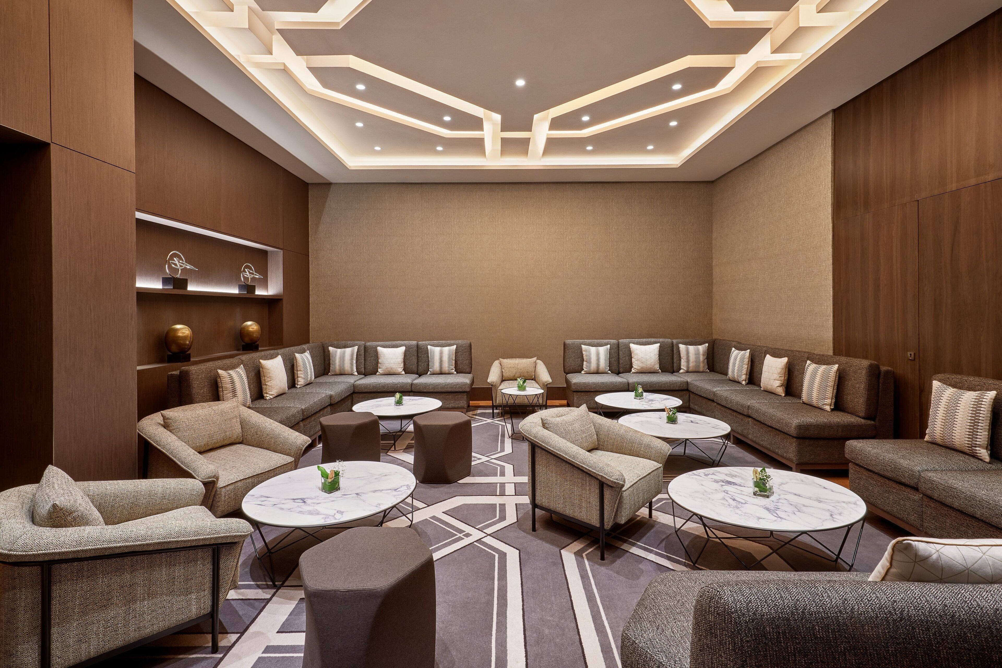 A modern lounge area with sofas, round tables, and a geometric ceiling design.