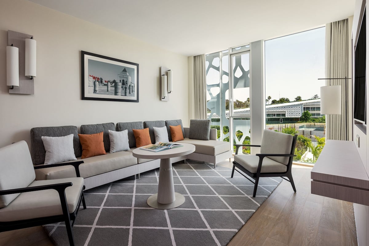 A modern living room with a sofa, armchairs, a coffee table, and a large window offering a view of a building and greenery.