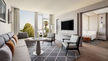 Une chambre d’hôtel moderne dotée d’une grande fenêtre, d’un téléviseur à écran plat, d’un canapé, de deux fauteuils, d’une petite table et d’un lit.