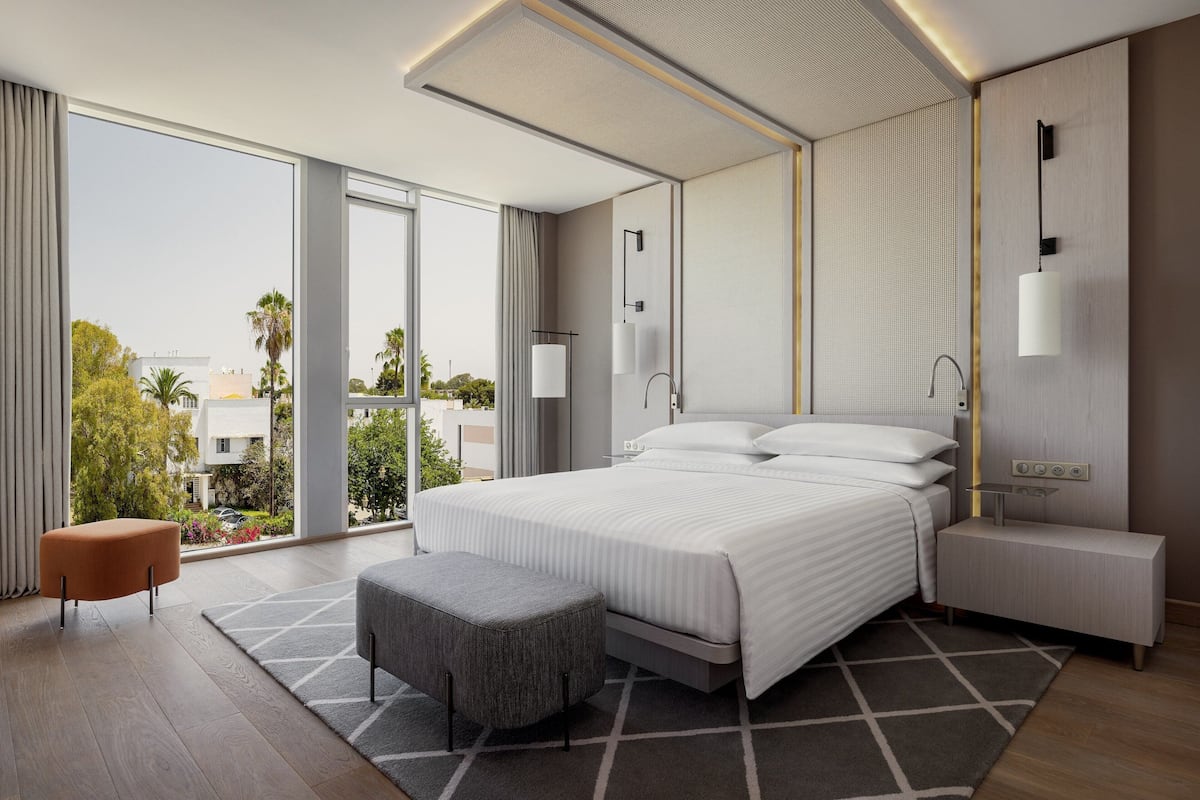 A modern hotel room with a large bed, a seating area, and a view of the outdoors.