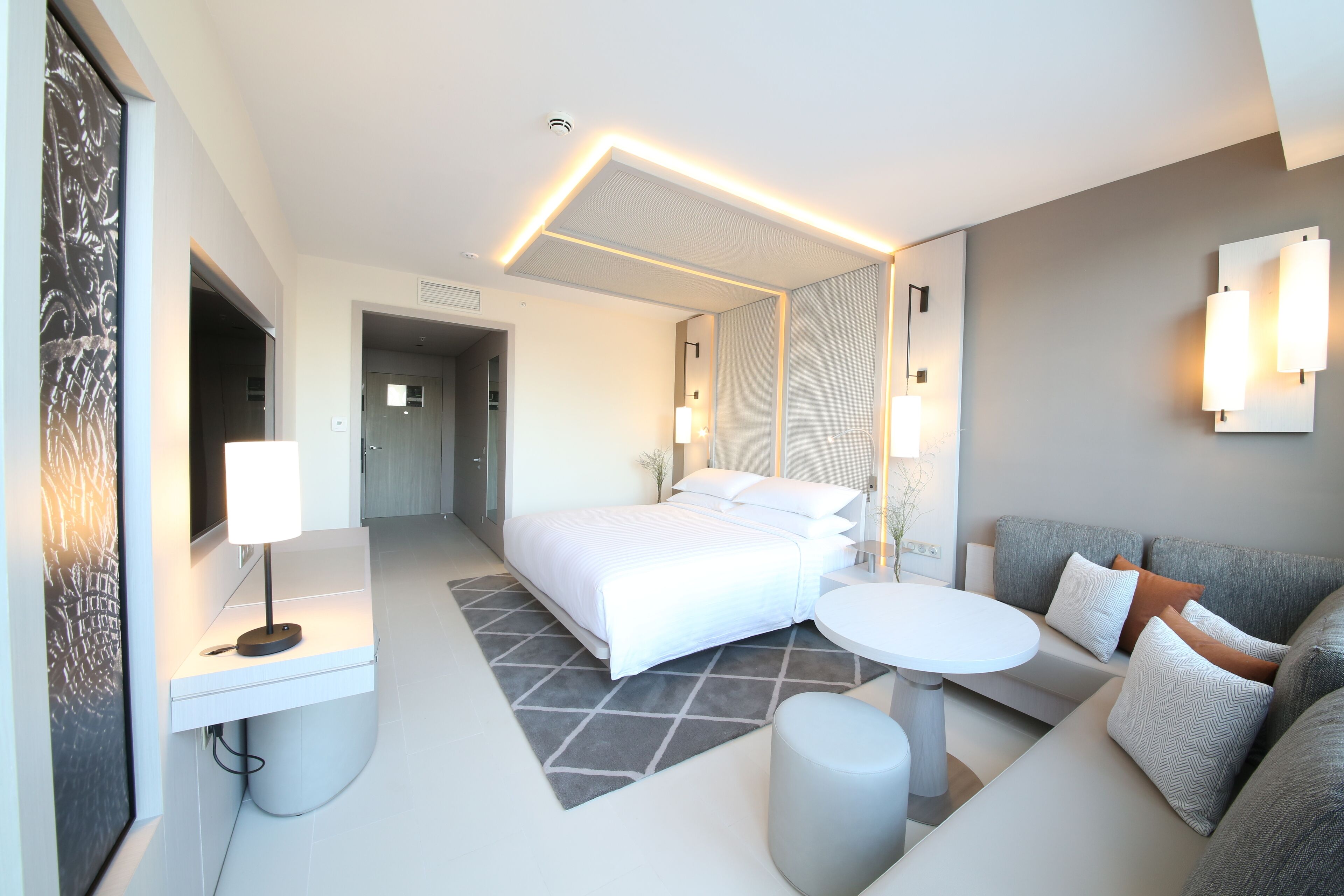 Une chambre d’hôtel moderne avec un lit, un canapé, une petite table et un miroir.