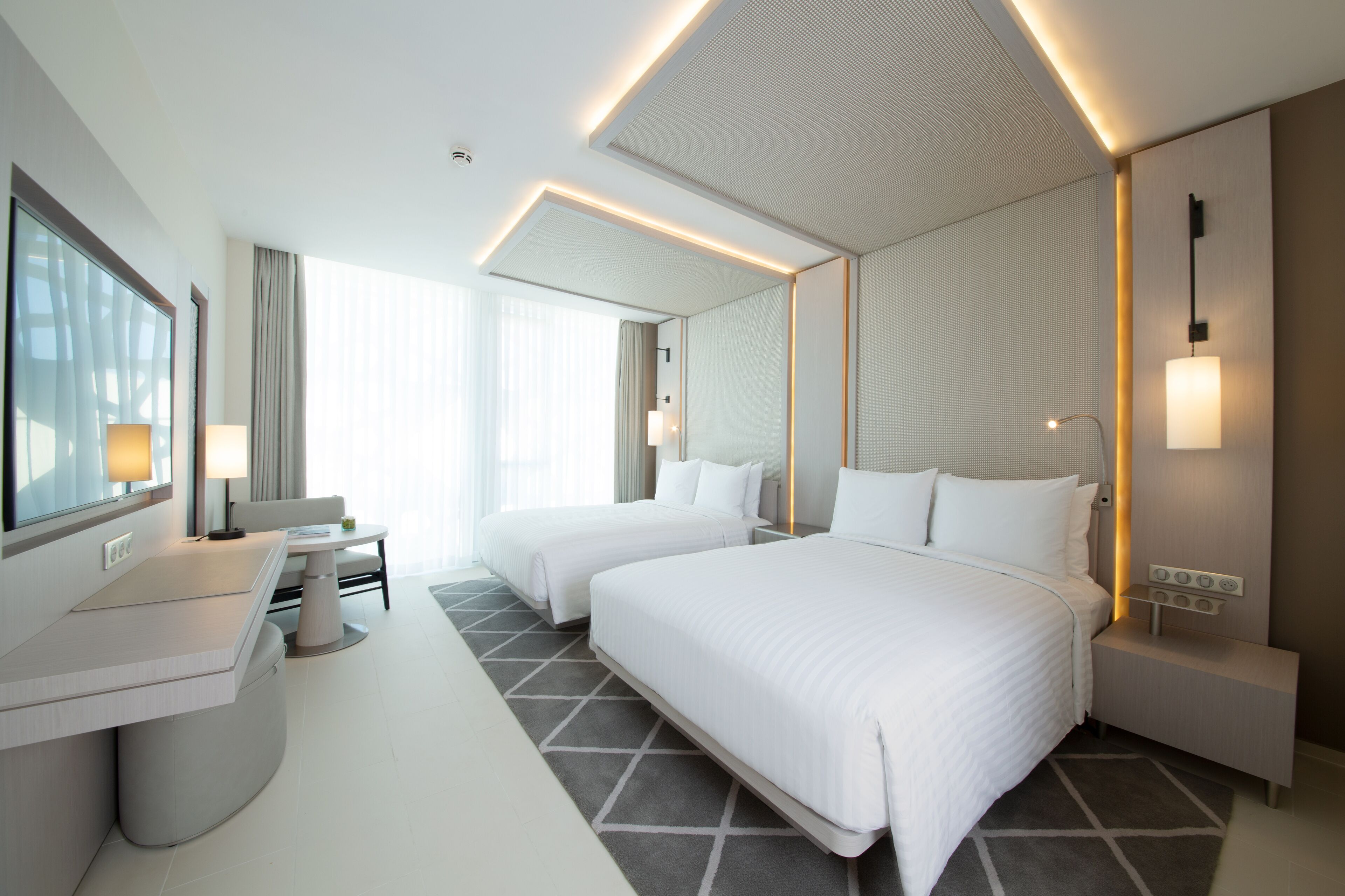 Ein modernes Hotelzimmer mit zwei Betten, einem Schreibtisch und einem großen Fenster.