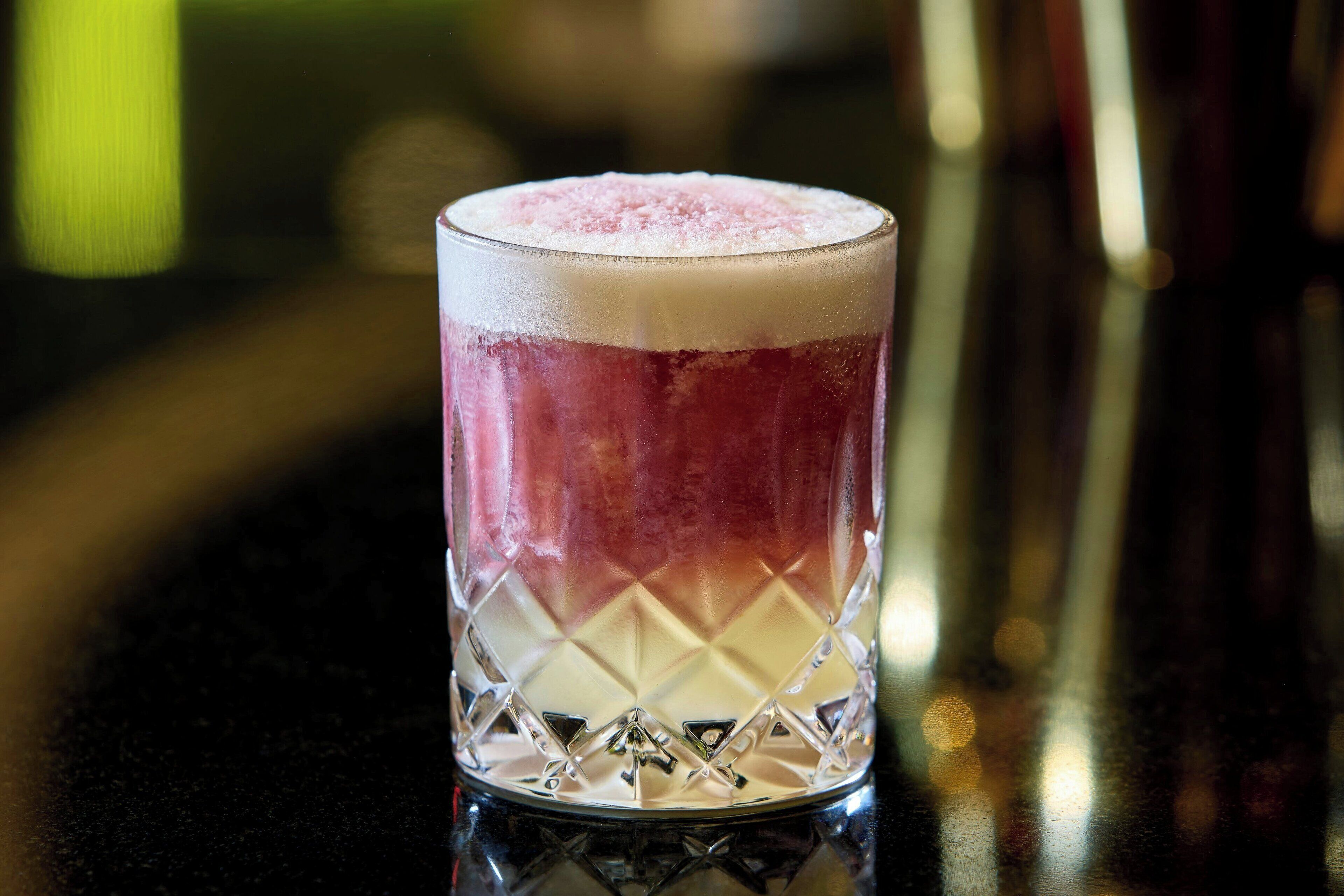 A glass with a layered drink, possibly a cocktail, on a reflective surface.