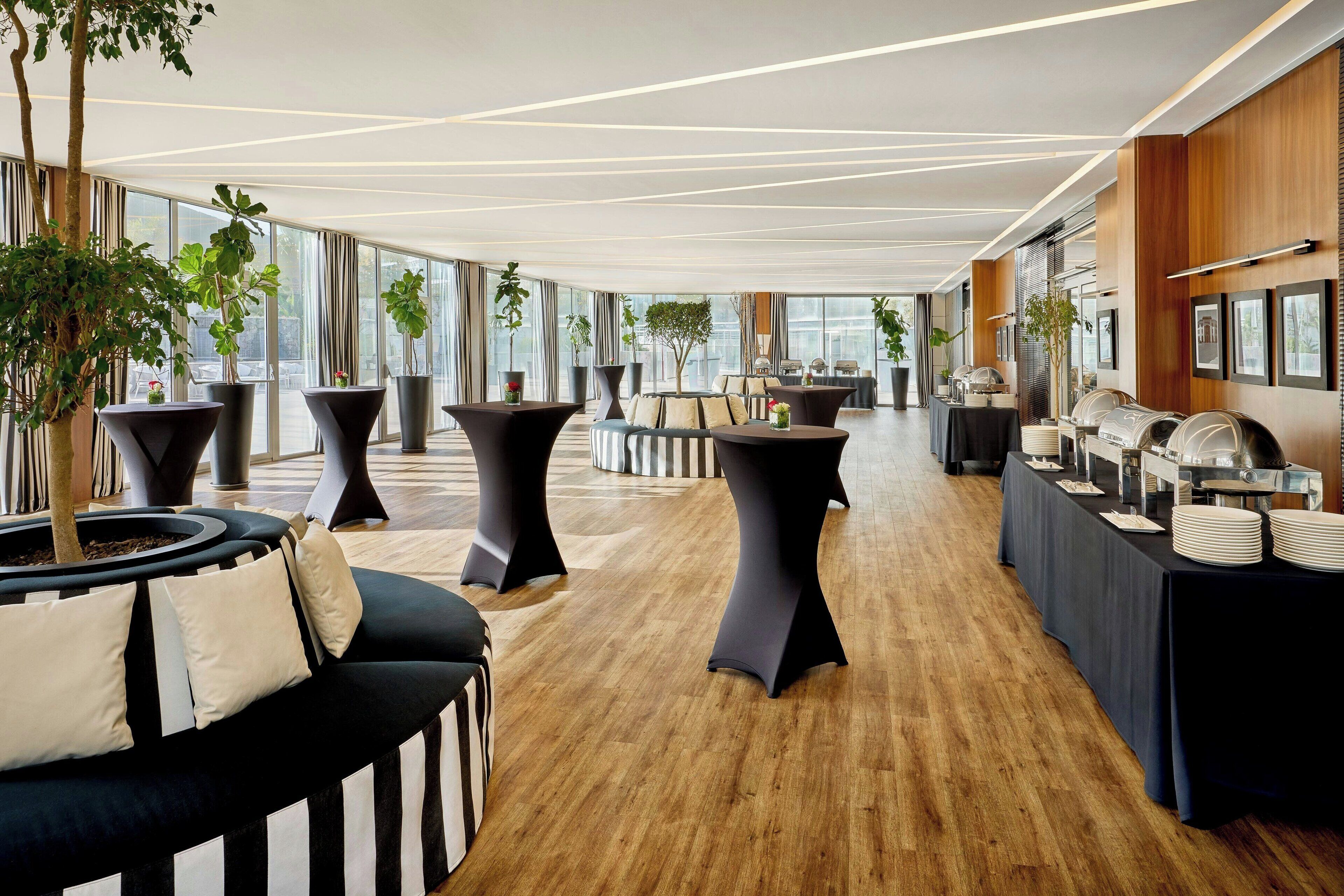 Un espacio interior moderno con una mesa larga, un sofá a rayas blanco y negro y plantas en macetas.