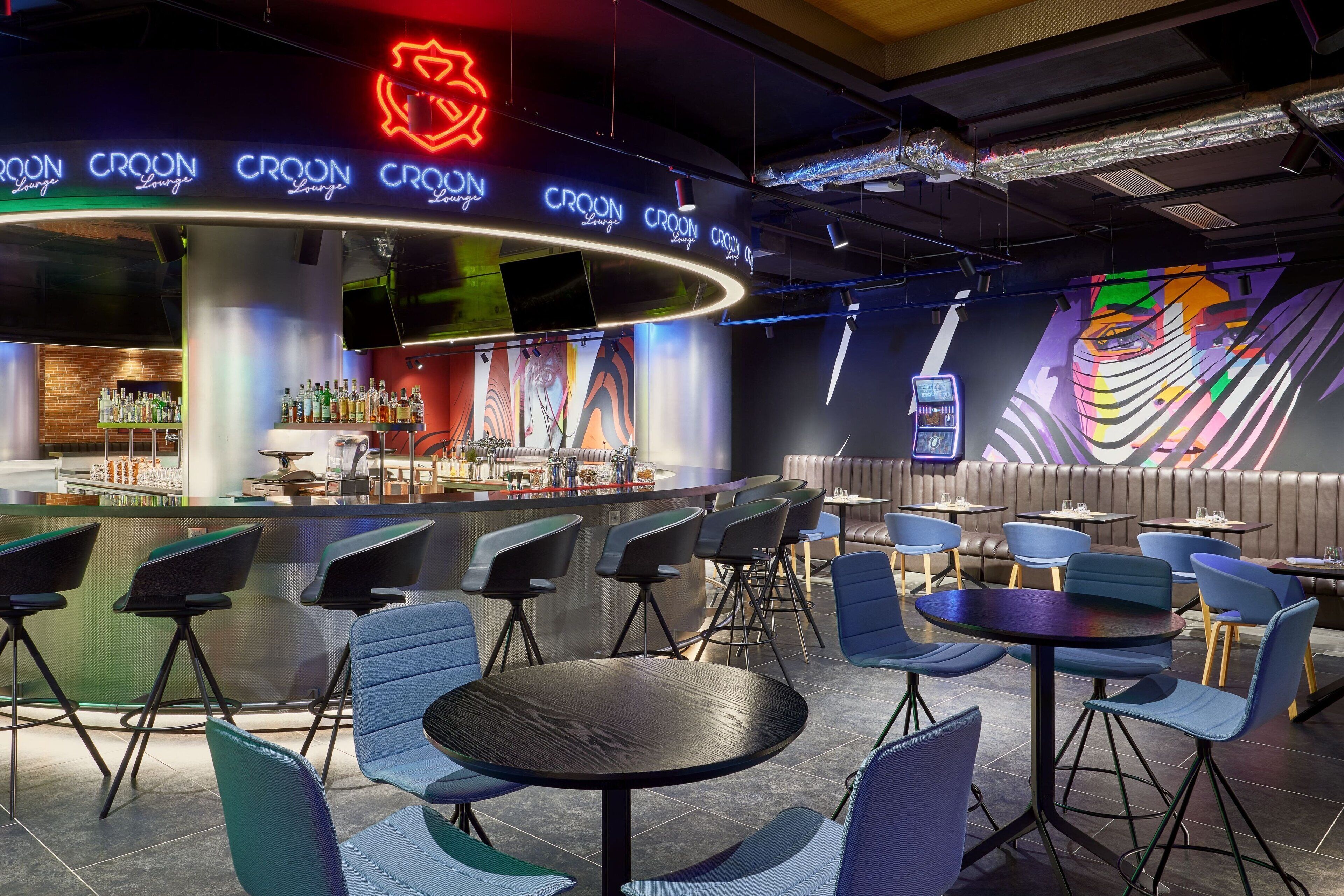 A modern bar area with neon signage, bar stools, and a seating area with tables and chairs.