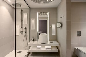 Features a sleek bathroom with a large mirror, glass-enclosed shower, and towel shelf.