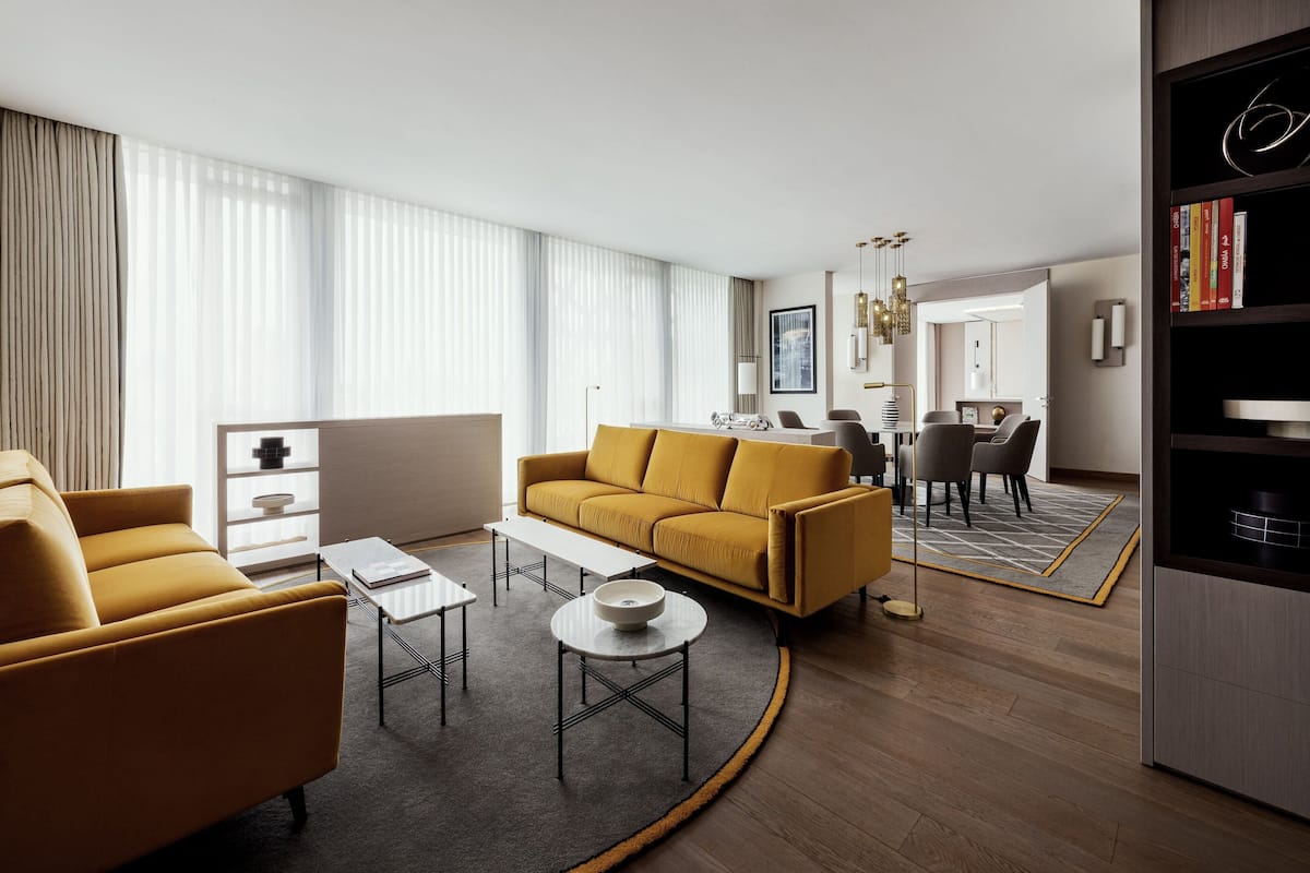 A modern living room with a yellow sofa, a coffee table, and a dining area in the background.