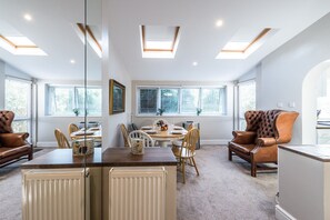 A spacious dining area with a high ceiling, skylights, and large windows with blinds.