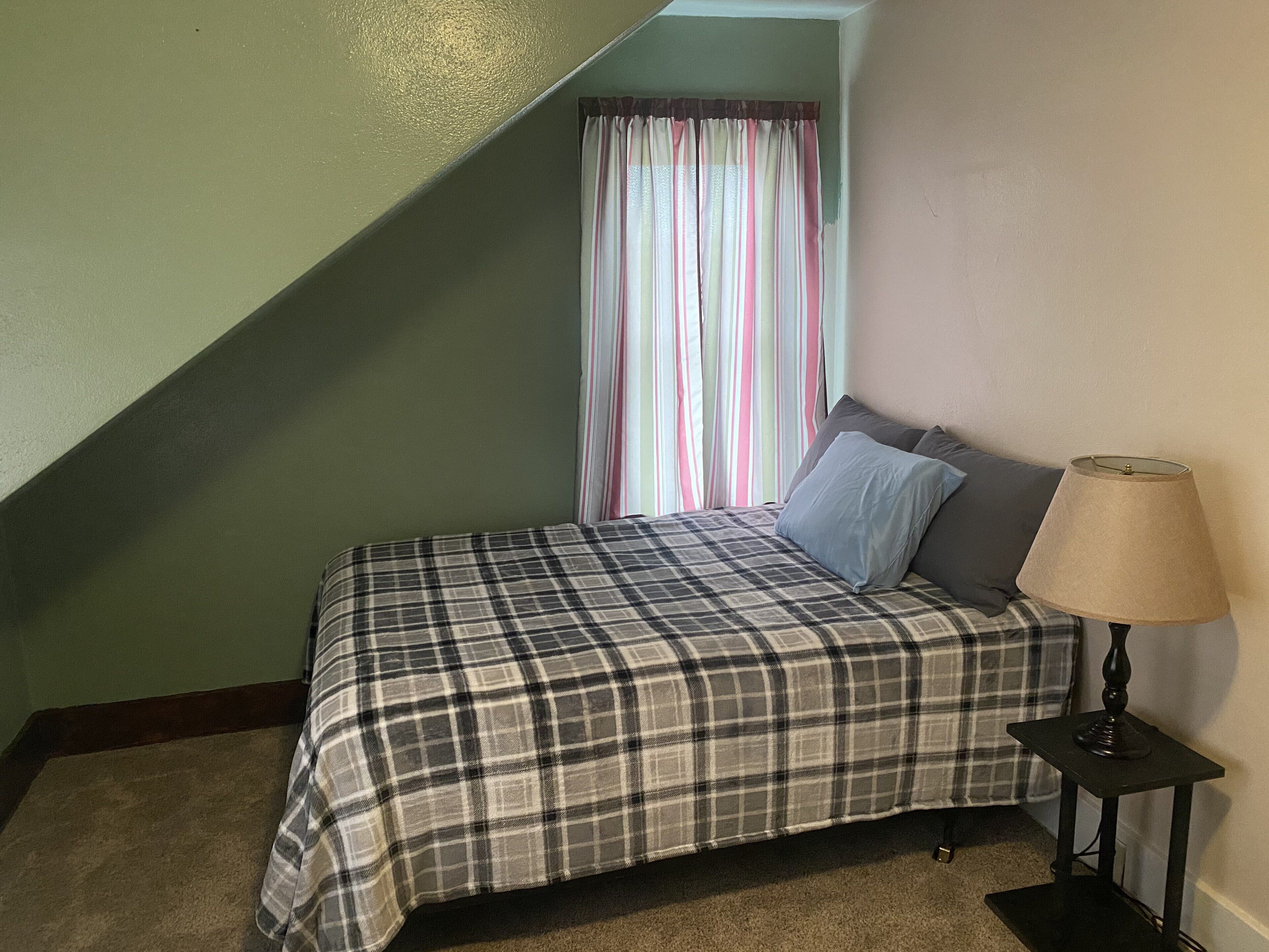 A bedroom with a bed, a lamp, and a window with curtains.