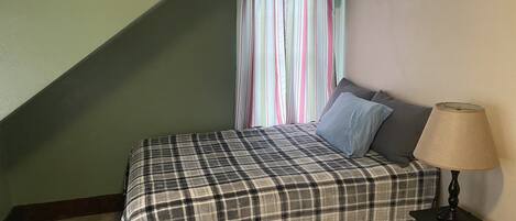 A bedroom with a bed, a lamp, and a window with curtains.