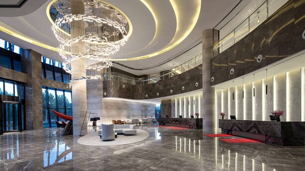 A spacious lobby with a modern chandelier, a reception desk, and seating areas.