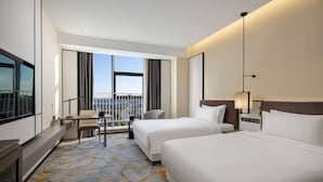 A hotel room with two beds, a desk, a chair, and a balcony with a view.