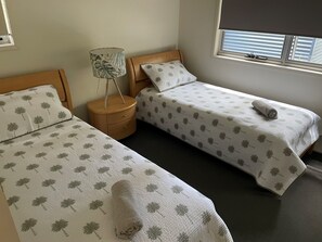 A bedroom with two single beds, each with a patterned bedspread and matching pillows. There is a wooden nightstand with a lamp between the beds. - Private self-contained Beachshack (Casuarina)
