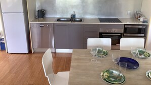 Una cocina moderna con electrodomésticos de acero inoxidable, armarios blancos y un comedor con una mesa de madera dispuesta para cuatro.