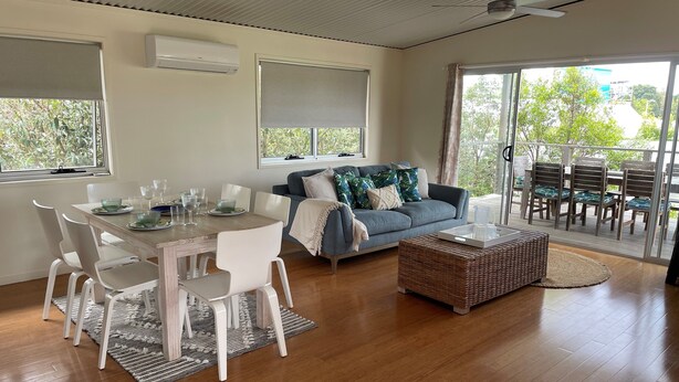 Una sala de estar moderna con comedor, un sofá, una mesa de centro y un balcón con mobiliario exterior.