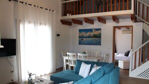 Een woonkamer met een blauwe bank, een eettafel met stoelen, een schilderij aan de muur en een trap.