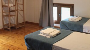 Een kamer met twee bedden, houten balken, een ladder en een raam met gordijnen.