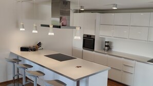 A modern kitchen with white cabinets, a central island with bar stools, a built-in oven, and a coffee machine. - Vacation apartment on the Haldershof ground floor (Wangen im Allgäu)