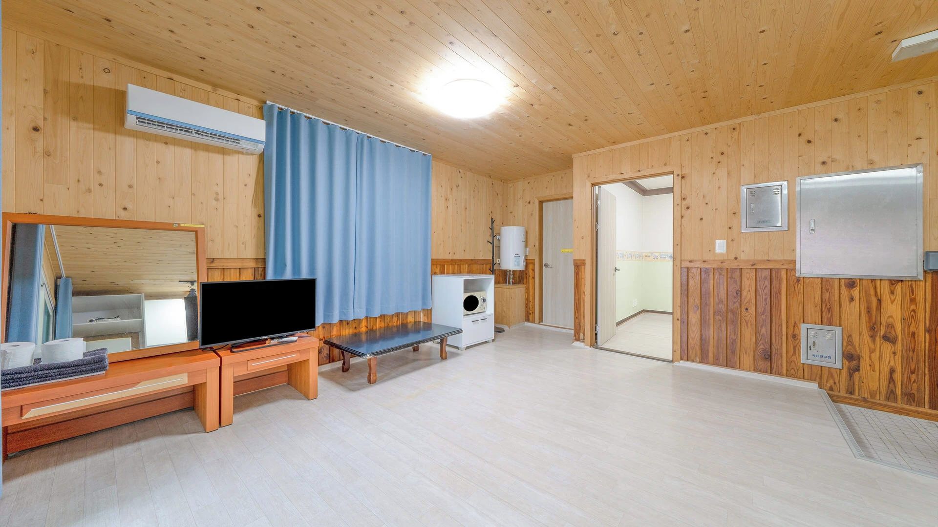 A room with wooden walls, a flat-screen TV, a bench, a washing machine, and a door leading to another room.