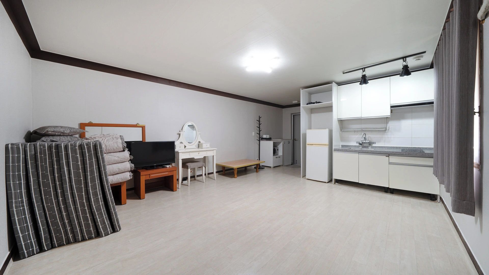 A compact living space with a kitchenette, a television, a desk, and a bed.