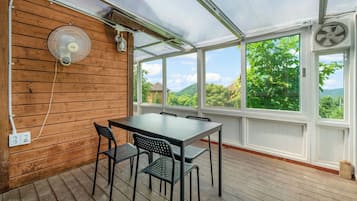Una habitación con paneles de madera, una mesa, sillas, ventanas amplias y un ventilador.