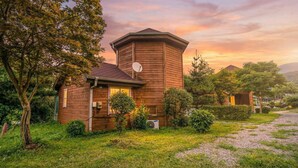 A wooden cabin with a satellite dish, surrounded by lush greenery and a gravel path. - Paju Gamaksan Sanchon Village Pension (Paju)