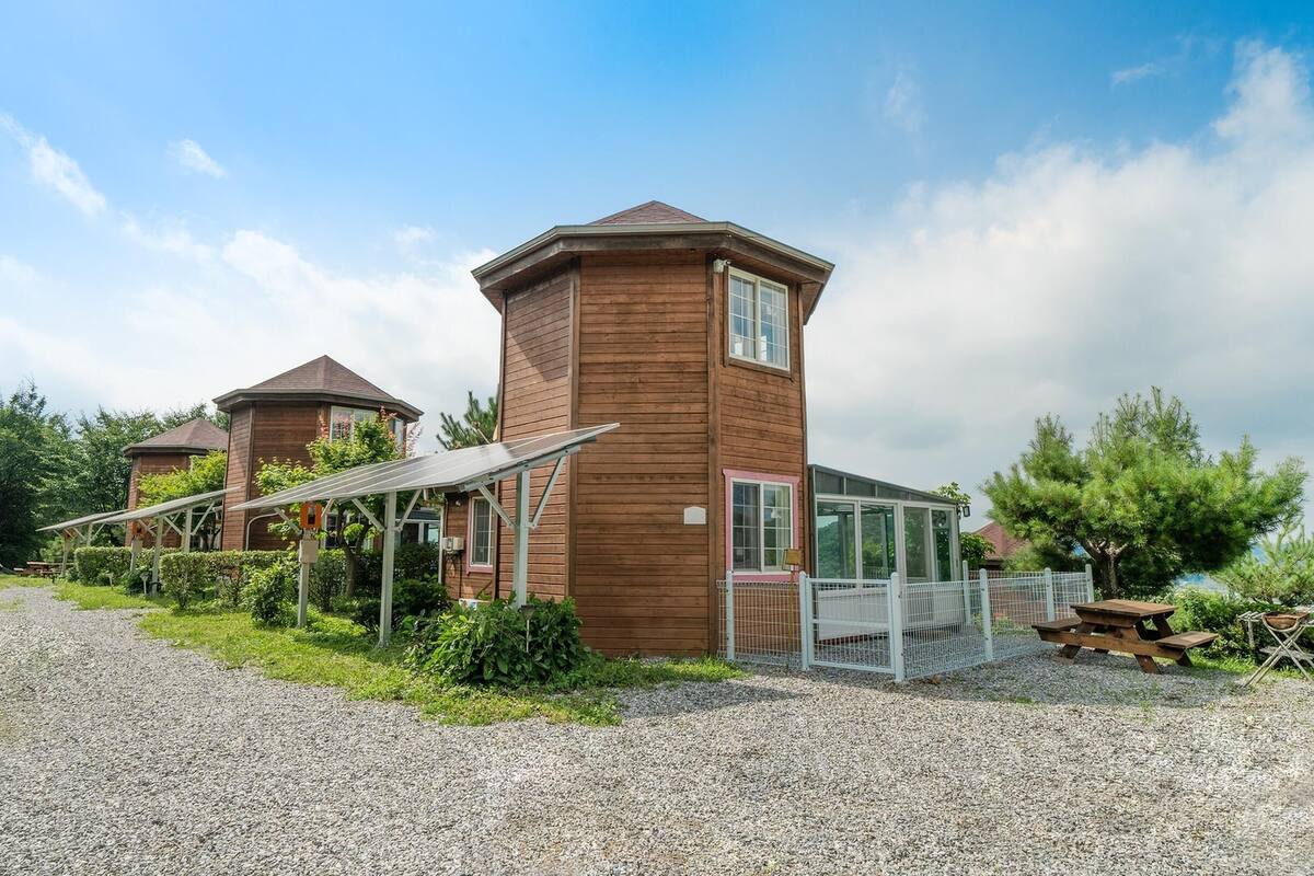 Eine Holzhütte mit einer Solaranlage, einem eingezäunten Bereich und einem Kiesweg.