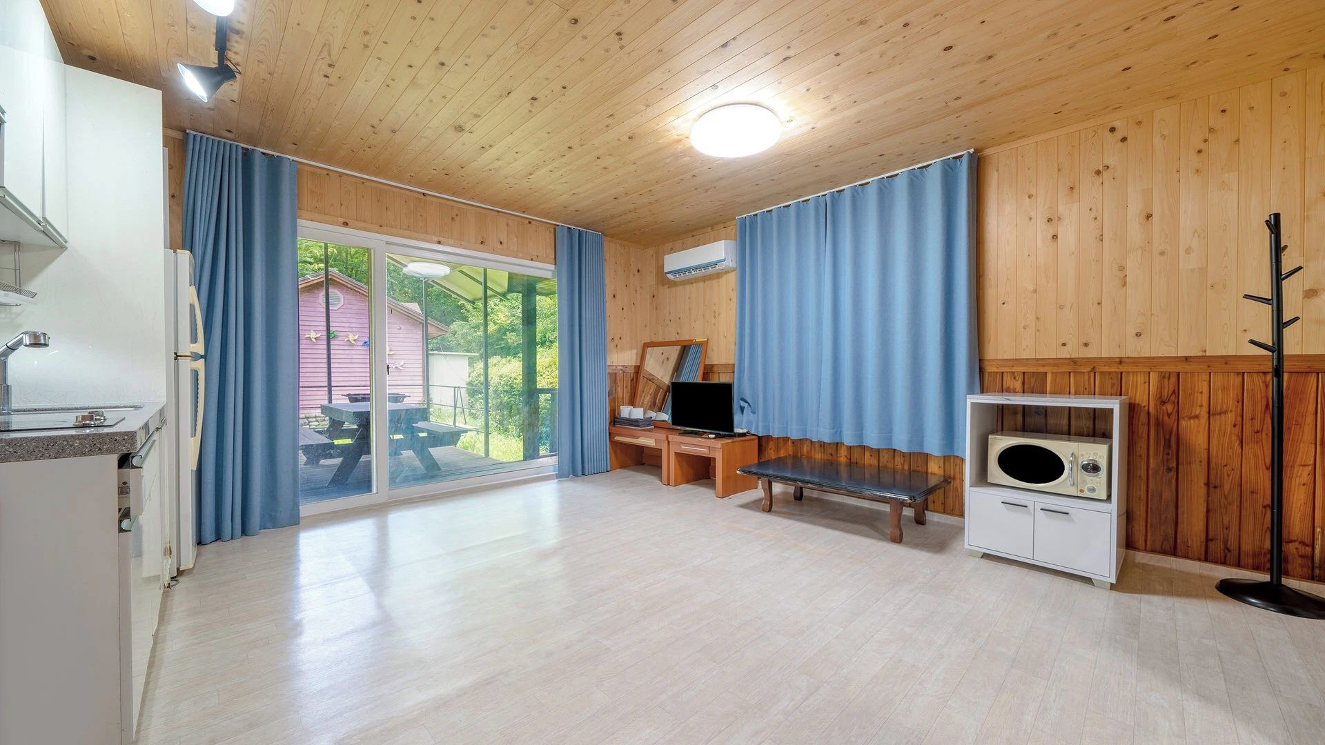 A room with a wooden ceiling, a television, a bench, a coat rack, and a window with curtains.