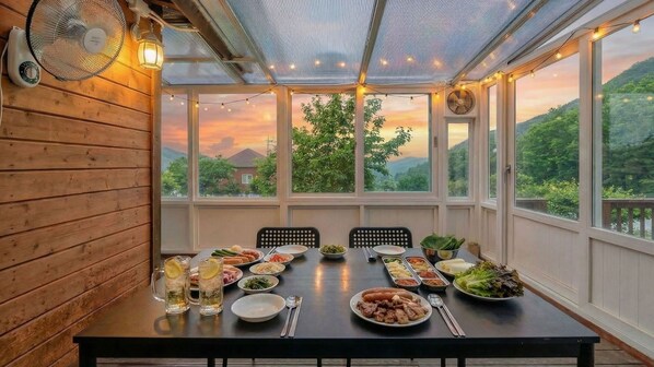 A covered dining area with a table set for a meal, large windows, and a view of the outdoors.