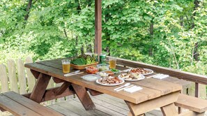 An outdoor wooden picnic table with various food items and drinks, surrounded by a lush green garden. - Paju Gamaksan Sanchon Village Pension (Paju)