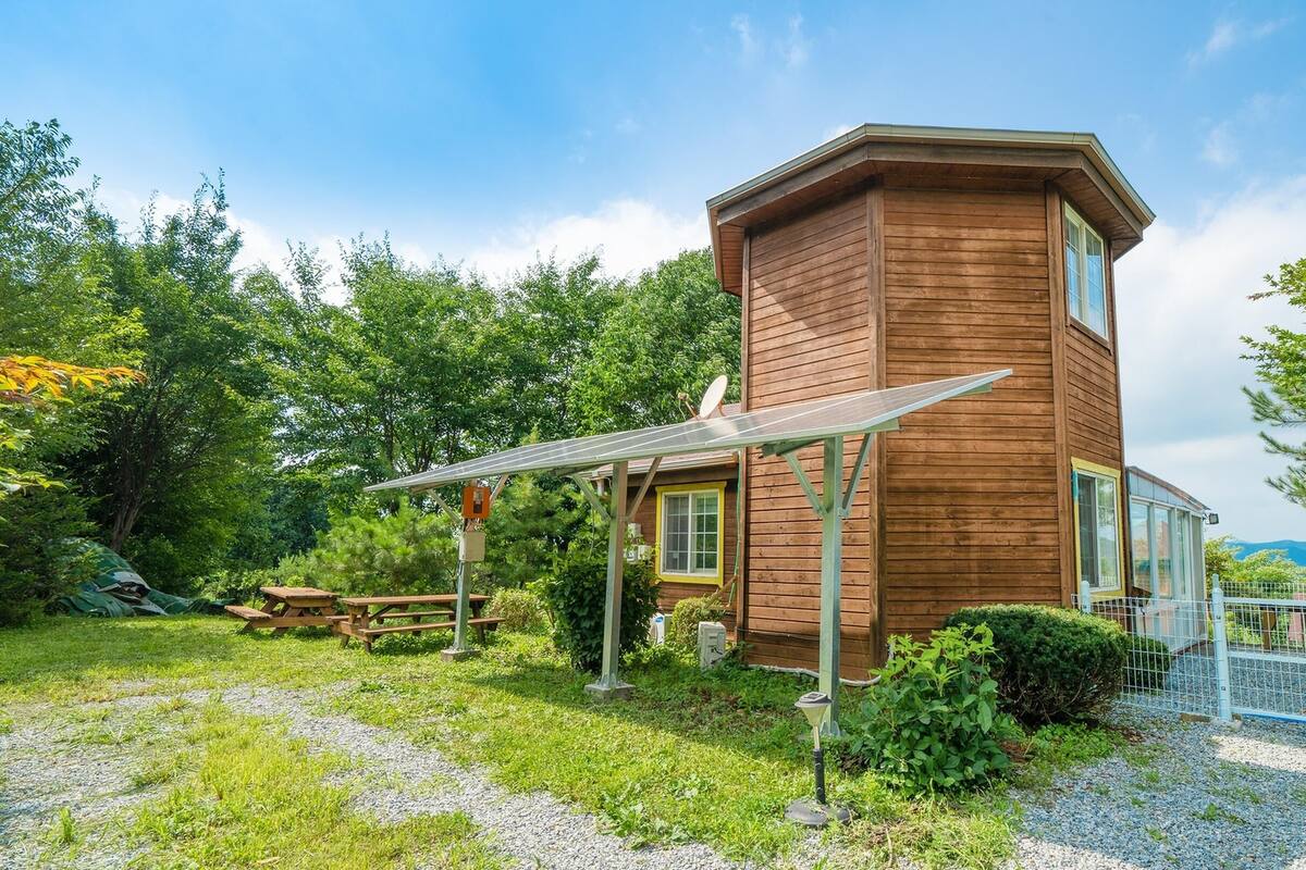Eine Holzdiele mit einer Solaranlage, umgeben von einem Garten und einem Kiesweg.