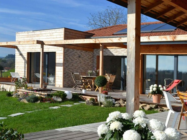 Une maison moderne dotée d’une terrasse en bois, d’un espace salon extérieur et d’un jardin.