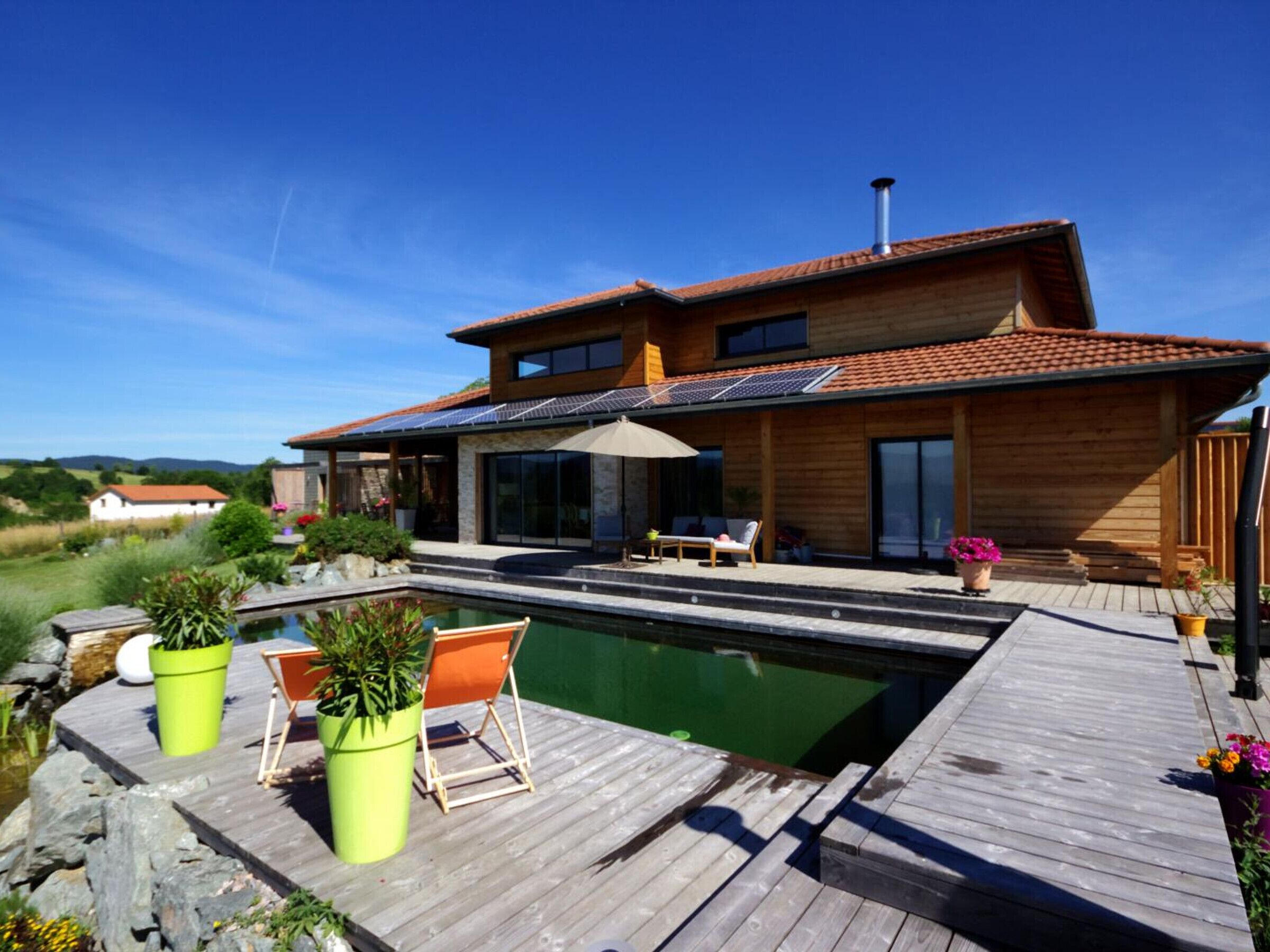 A modern house with a swimming pool, wooden deck, and outdoor seating area.