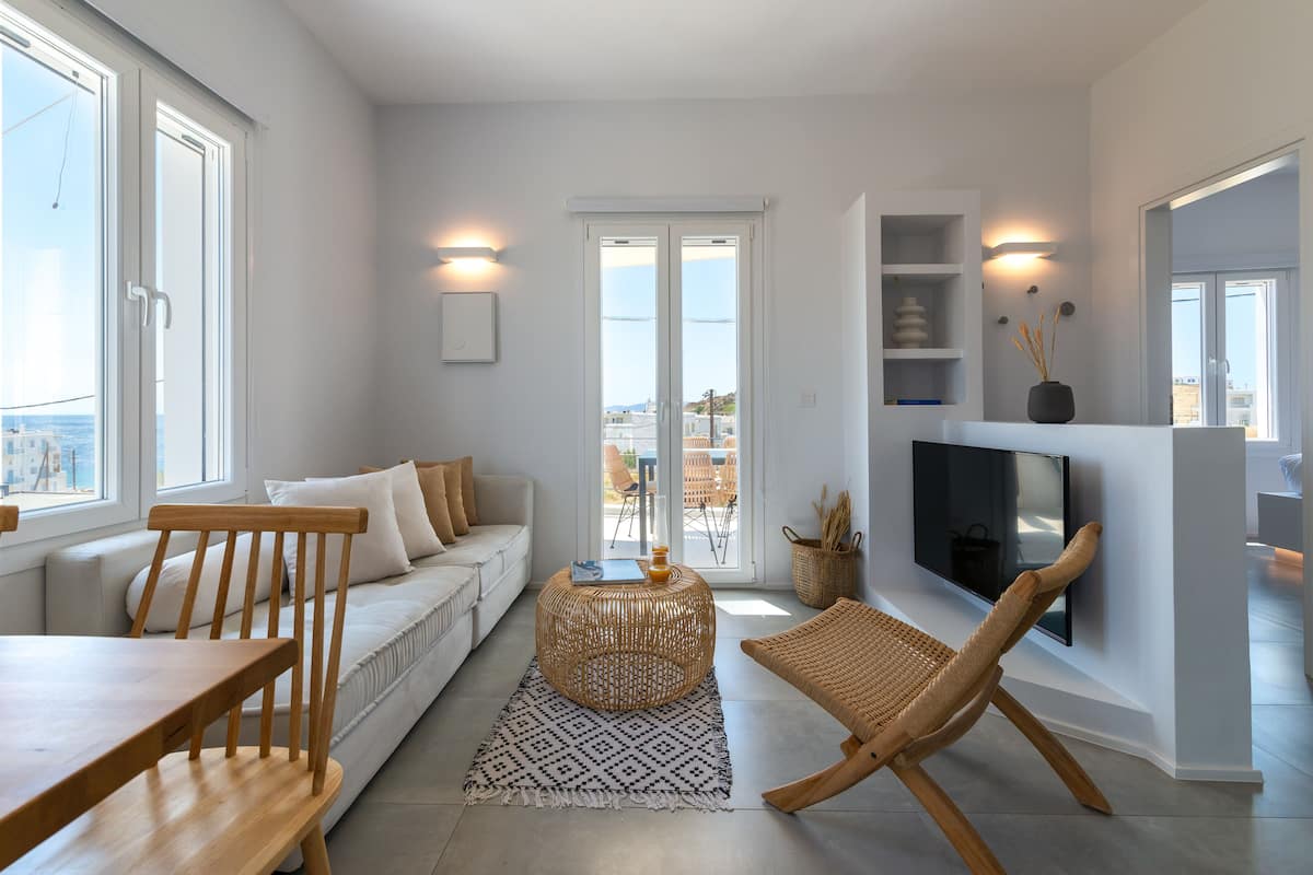Een moderne woonkamer met een bank, een ronde salontafel, een aan de muur bevestigde televisie, en een eethoek met een houten tafel en stoelen.