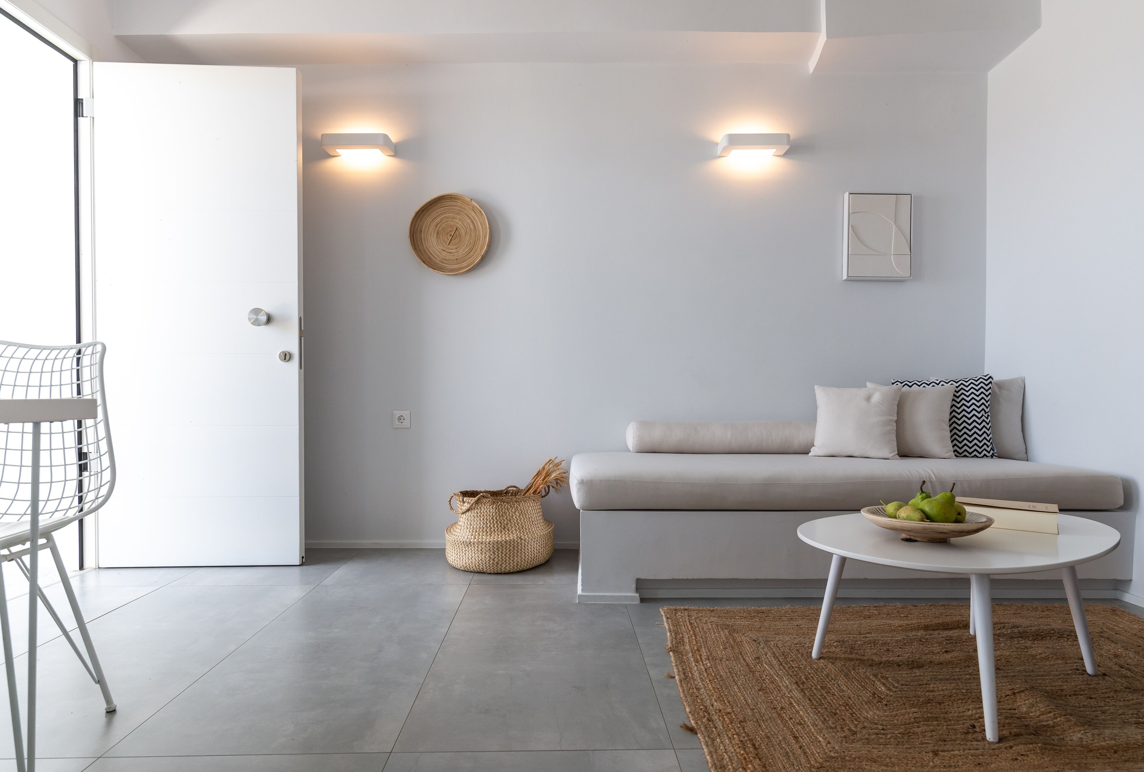 Una sala de estar moderna con un sofá gris, una mesa redonda de centro con un cuenco de frutas, una cesta tejida y una silla blanca.
