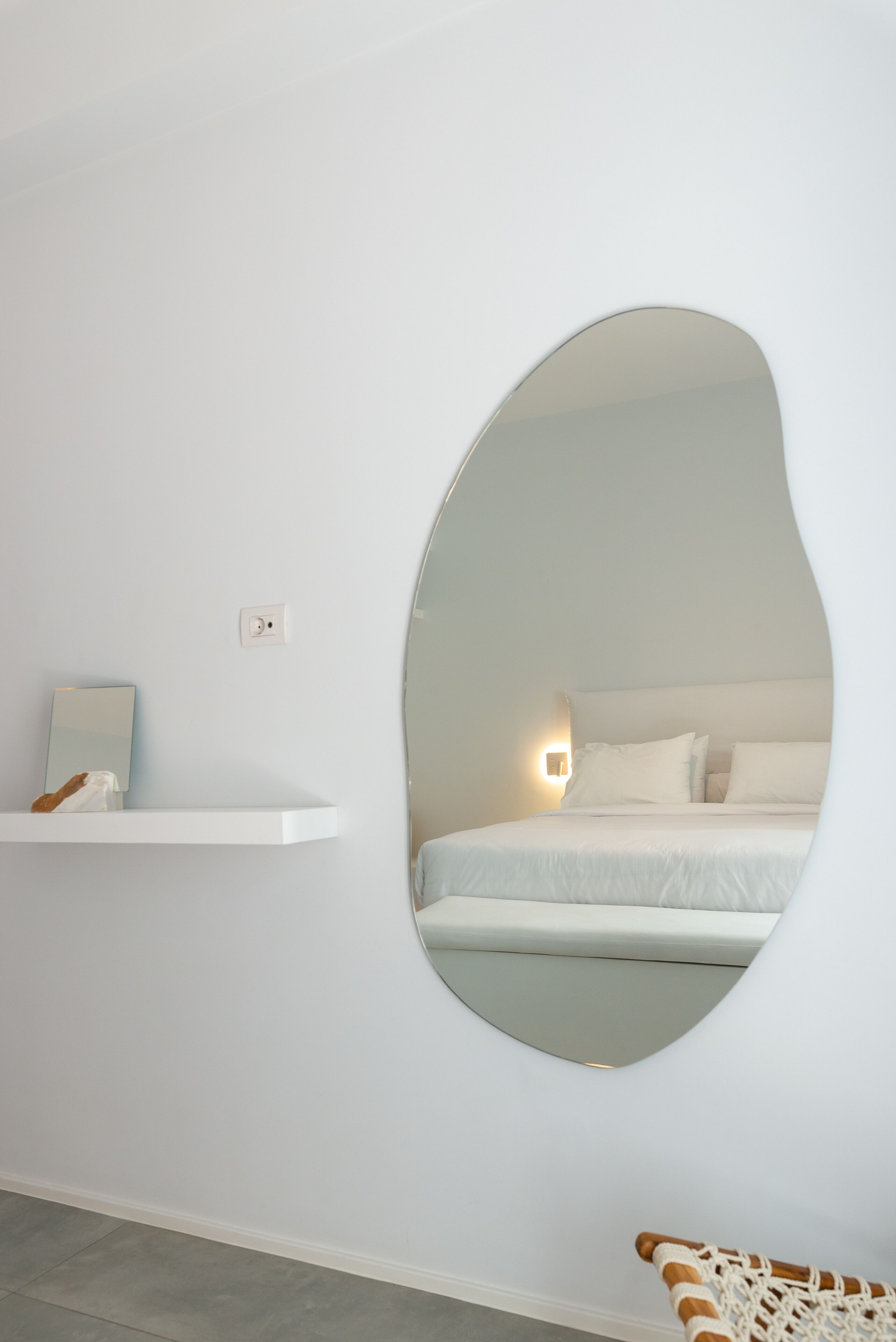 Camera da letto con un ampio specchio ovale, un comodino e un letto con biancheria bianca.