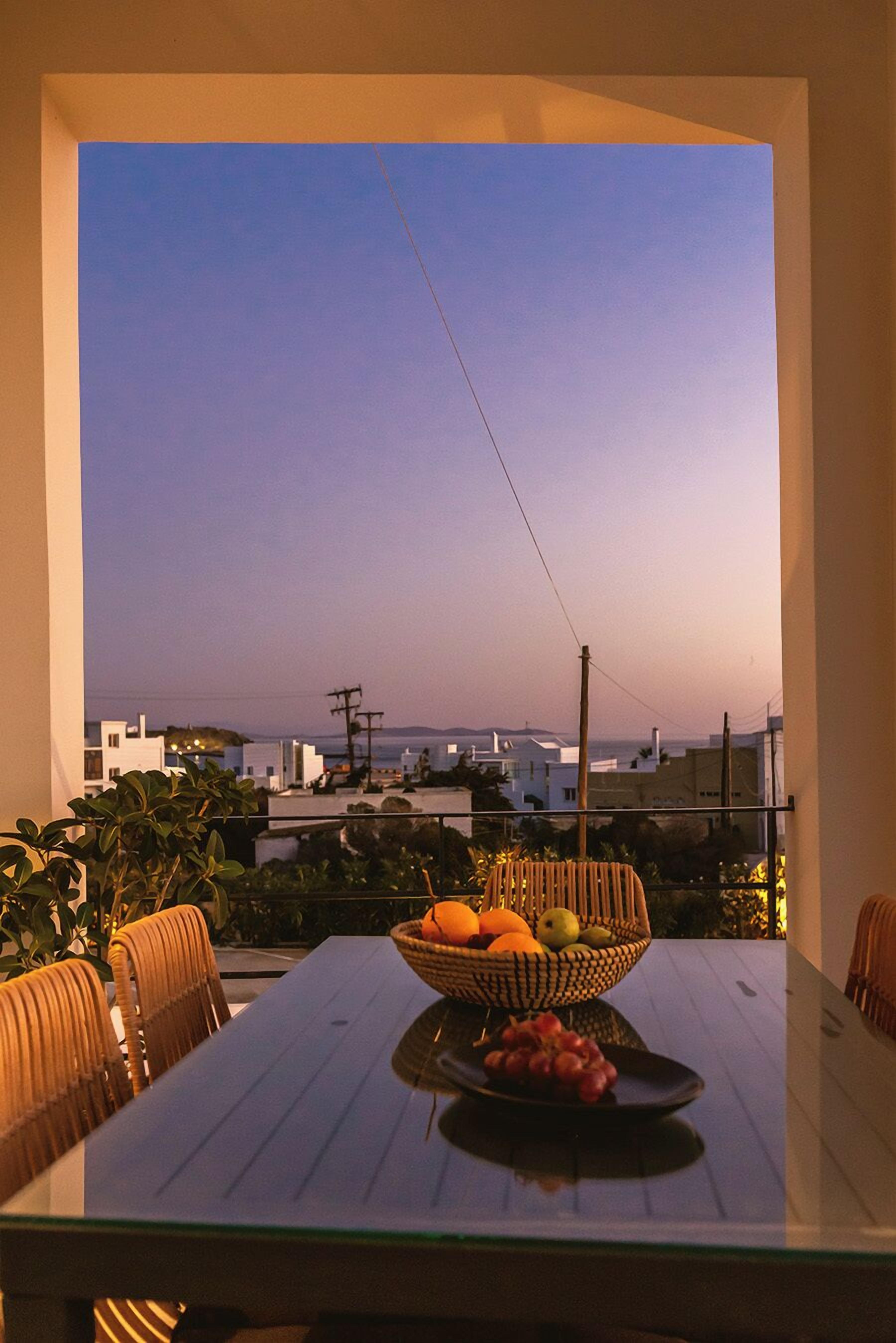A dining table with a fruit bowl and grapes, overlooking a cityscape at dusk.