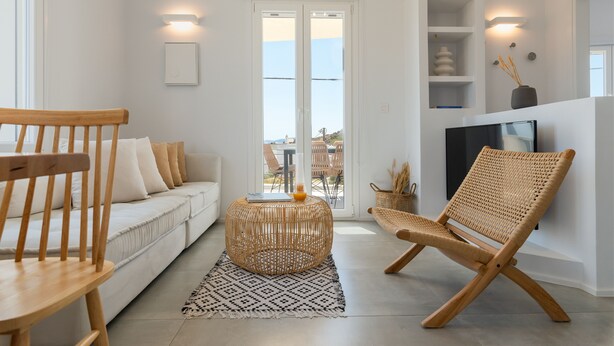 Een moderne woonkamer met een witte bank, een houten stoel, een geweven salontafel en een televisie op een dressoir.