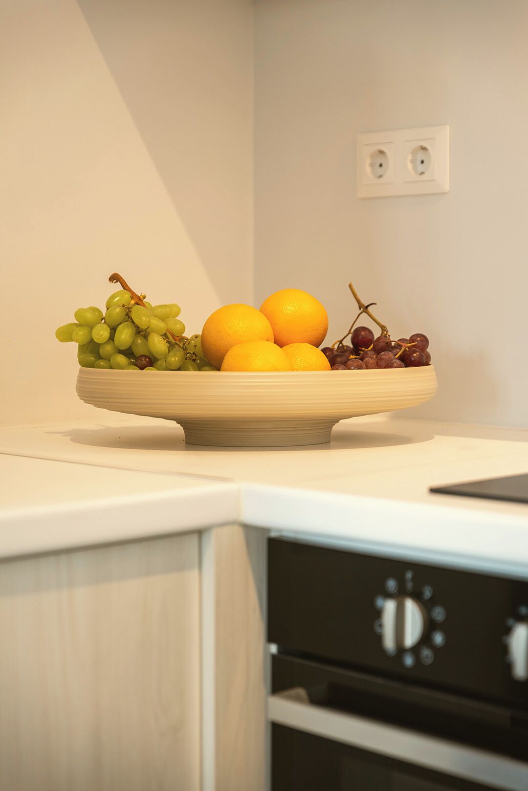 A fruit bowl on a kitchen counter with a white wall and a power outlet in the background.