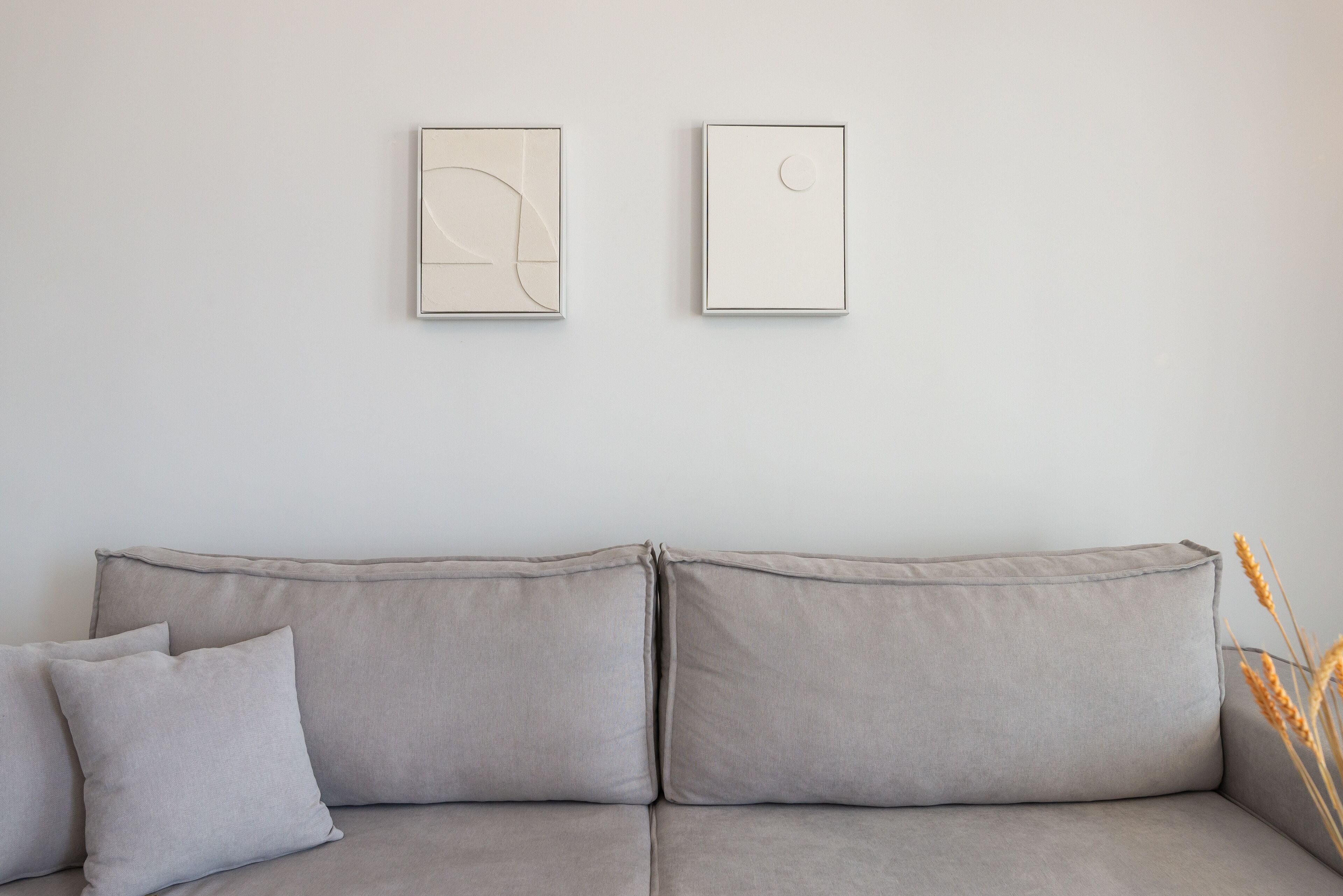 Un divano grigio con due cuscini e due quadri appesi al muro.
