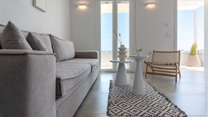 Een moderne woonkamer met een grijze bank, een kamerbreed tapijt met een patroon, een klein wit tafeltje en een geweven stoel.