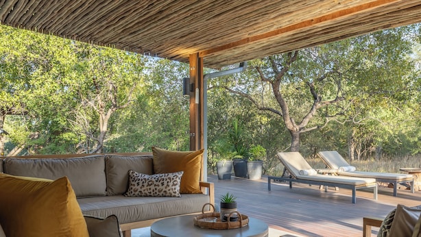 Un espace extérieur aménagé, abrité et doté d’une terrasse en bois, de chaises longues, d’un canapé avec des coussins et d’une table ronde avec un plateau.