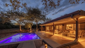 Une terrasse en bois avec une piscine, du mobilier d’extérieur et un intérieur éclairé.