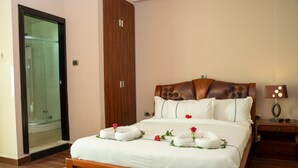 Una cama bien tendida con sábanas blancas y toallas decorativas, un cabecero de madera y una mesita de noche con una lámpara.