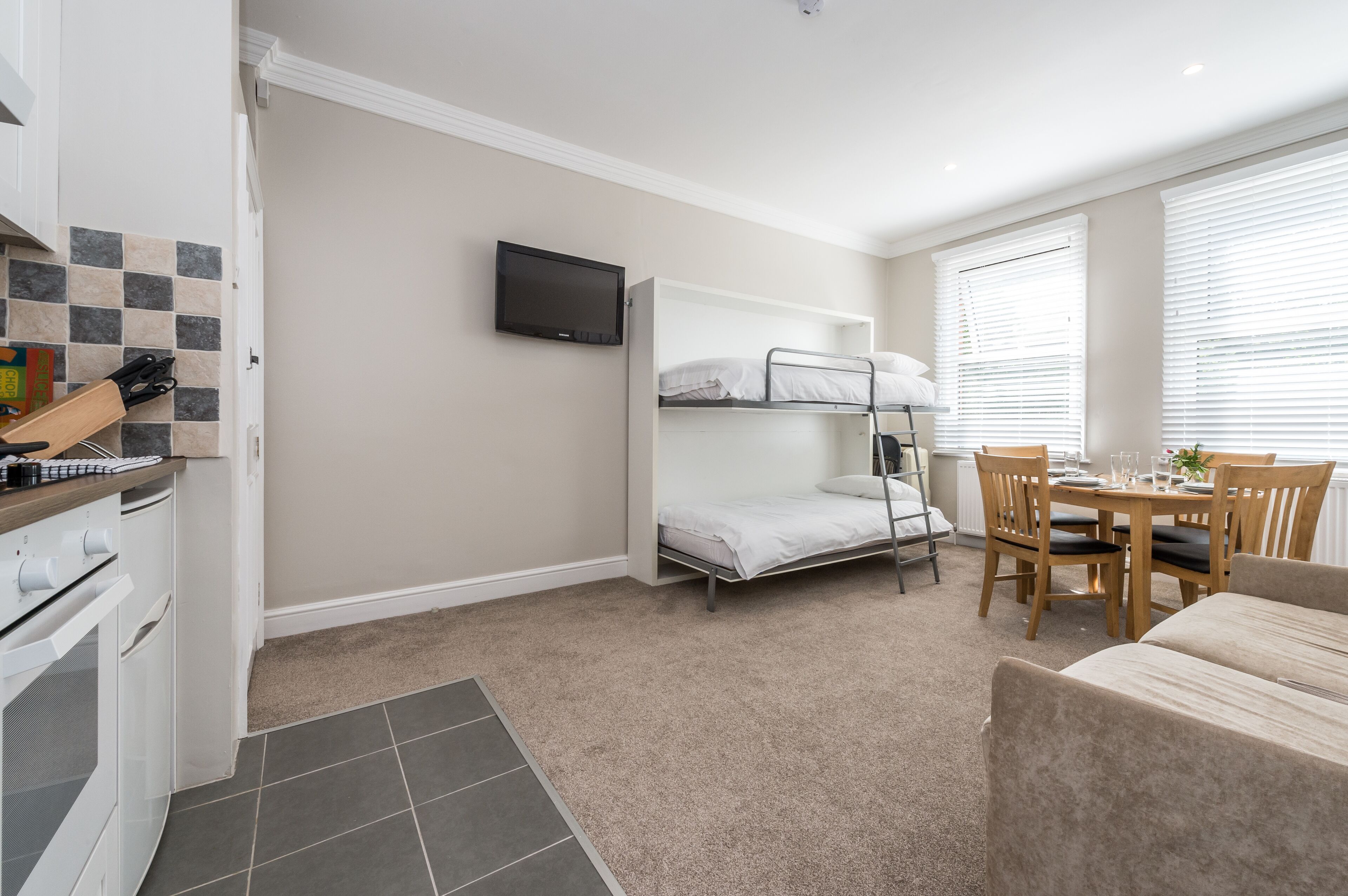 A compact room with bunk beds, a small kitchen area, a dining table, and a television.