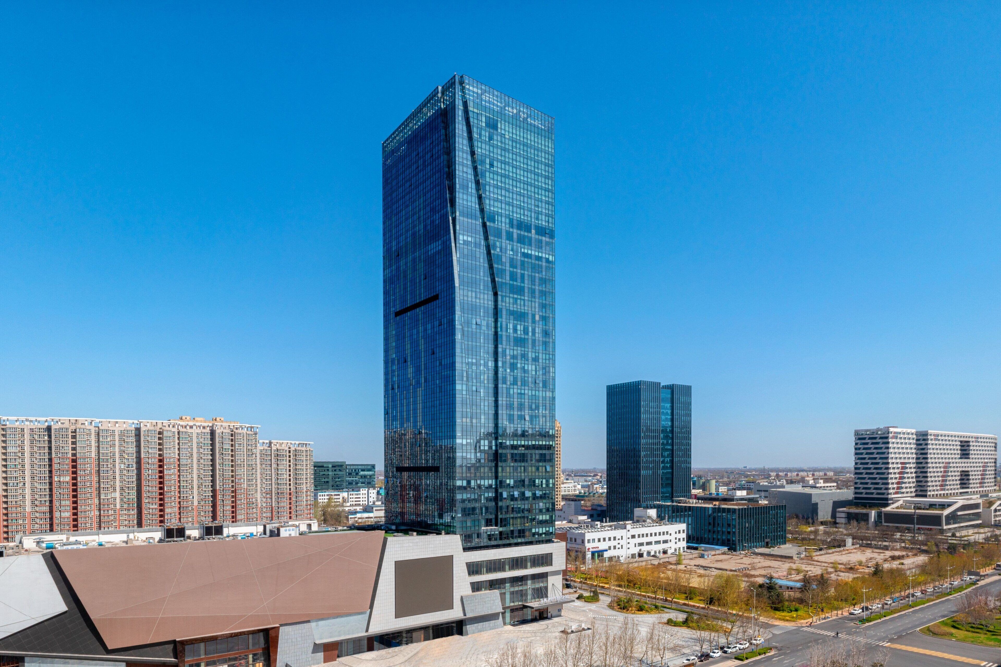 A modern high-rise building with a reflective glass facade, surrounded by other high-rise buildings and a clear blue sky.