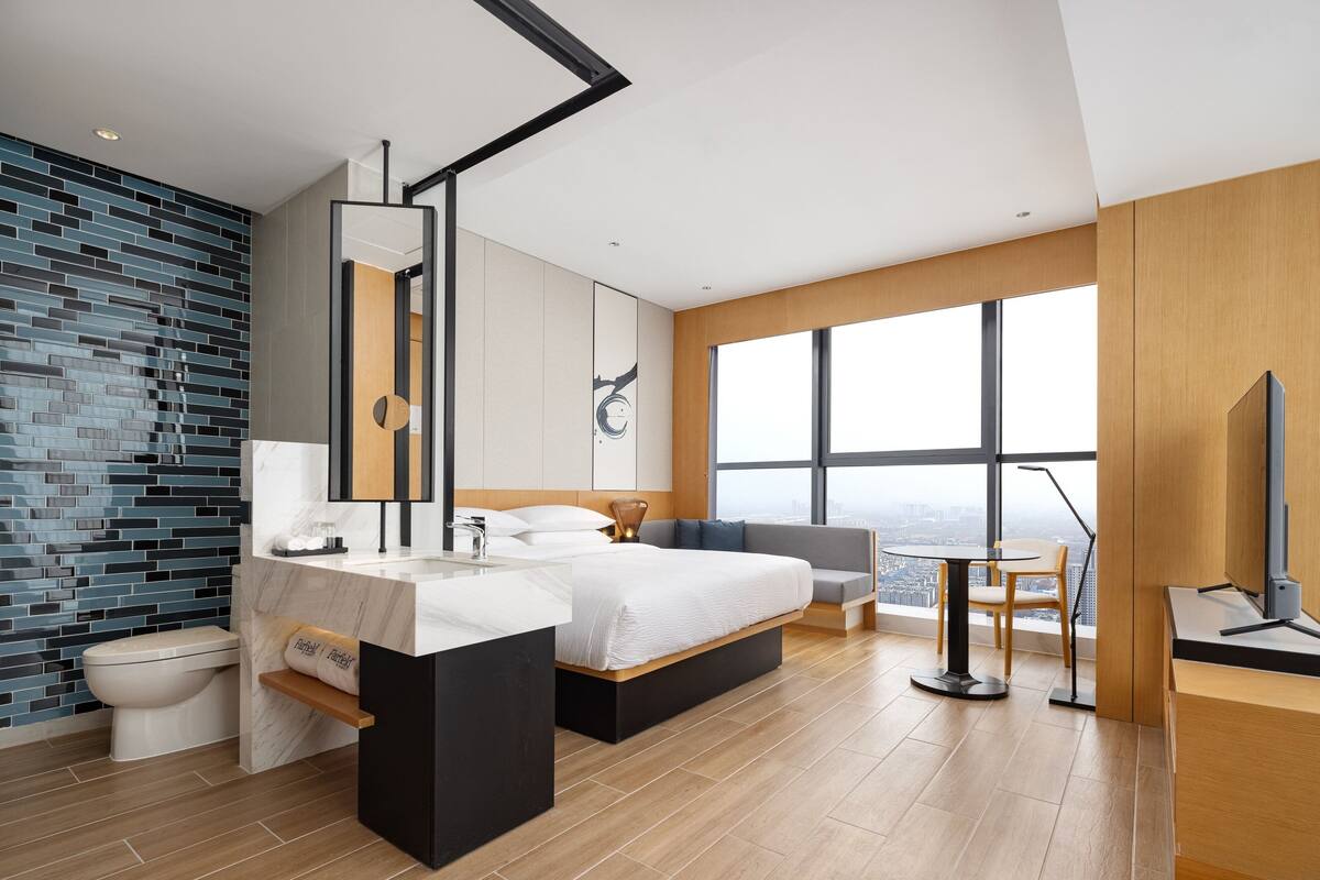 A modern bedroom with a large bed, a bathroom with a mirror, and a city view through large windows.