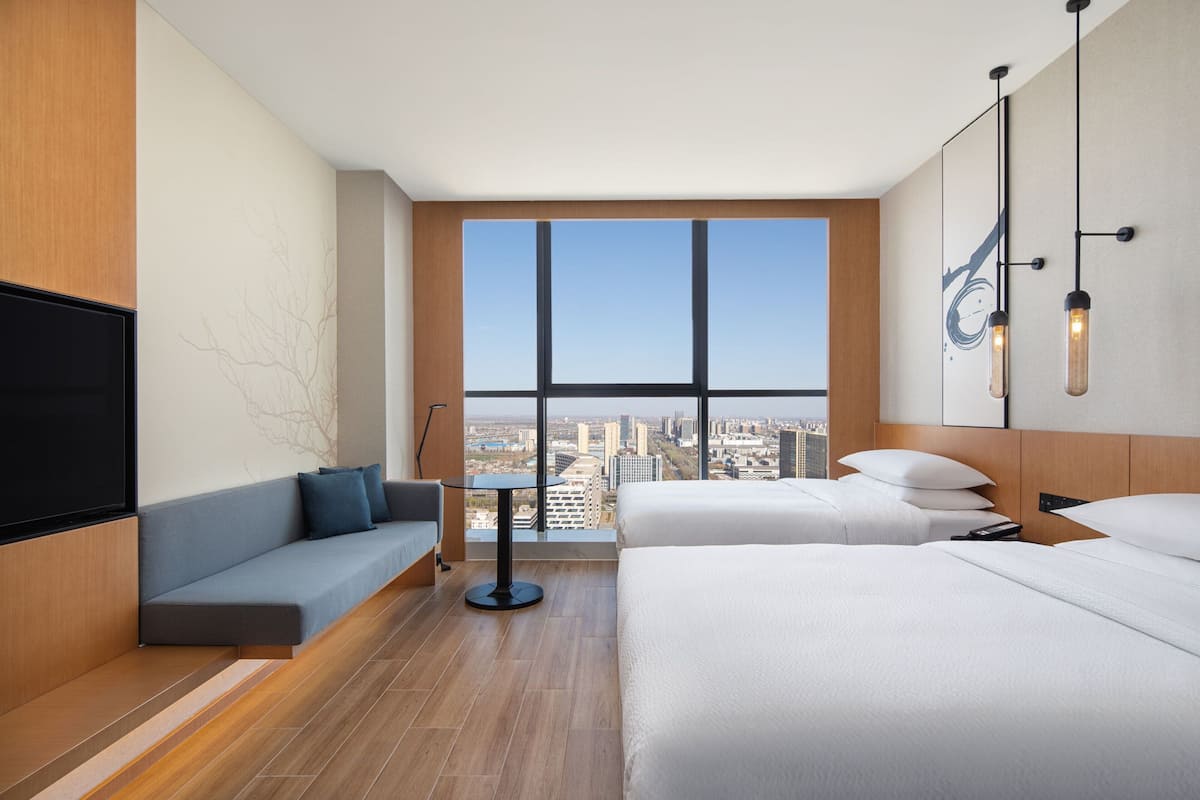 A modern hotel room with a large window, a sofa, a bed, and a flat-screen TV.