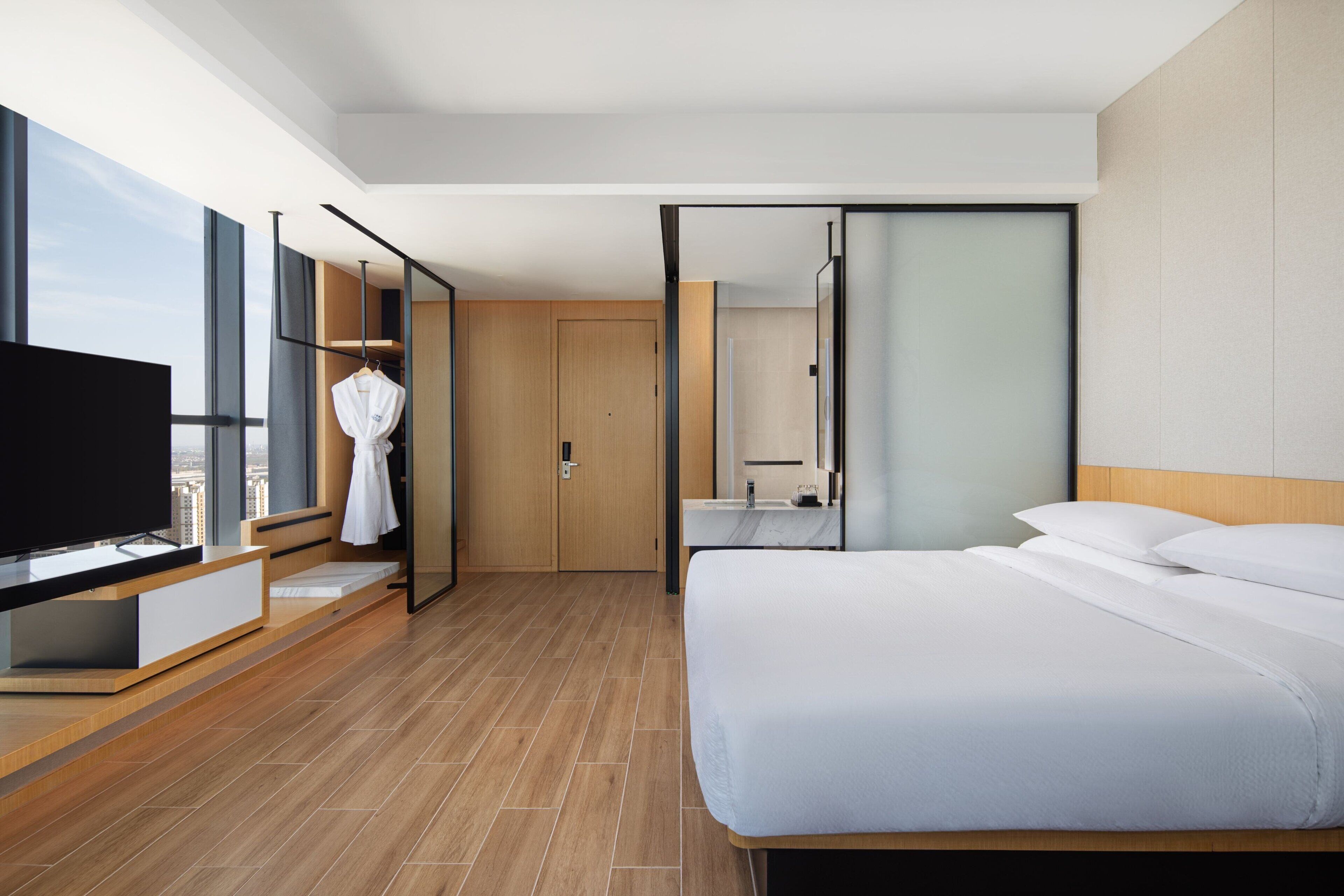 A modern hotel room with a large bed, a TV, a wardrobe, and a bathroom with a mirror.